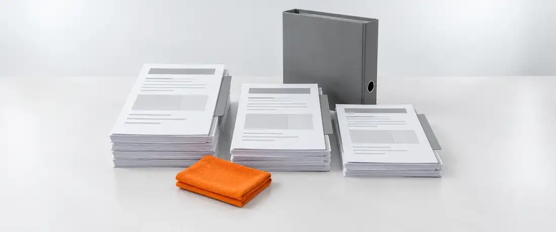 Pilhas de certificados de calibração com separadores cinza, lado a lado diante de uma pasta de arquivo fechada, na bancada